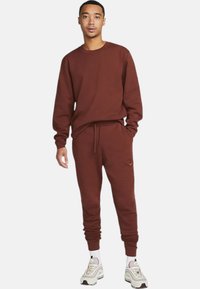 Maroon sweatpants and long-sleeve top made of cotton. Casual fit with elastic waist and cuffs, featuring a small logo accent on the top.