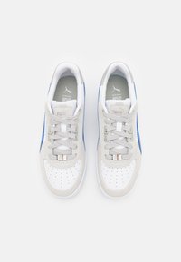 Vita sneakers med grå mockaaccenter, blå sidoremsor och perforerat tåområde. Har grå snören och en texturerad sula.