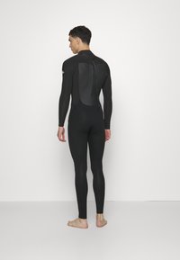 Muta nera con maniche lunghe, texture liscia, copertura completa del corpo e cerniera sul retro. Design aderente con aree rinforzate sulla schiena.