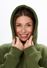 Olijfgroene hoodie met een grote, ronde capuchon en geribbelde manchetten. De stof oogt zacht en comfortabel, met een losse pasvorm.