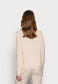 Beige gebreide trui met geribbelde manchetten en zoom, met een eenvoudig ontwerp en een gladde textuur. Draagt lichtgekleurde broek.