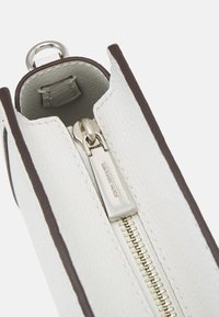 Bílá texturovaná kožená taštička s hnědým lemem, s kovovým zipem a vyraženým logem značky. Interiér je viditelný.