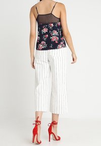 Camisola floreale navy con dettagli in rete, abbinata a pantaloni cropped bianchi a righe. Tacchi a spillo rossi con cinturini alla caviglia completano il look.