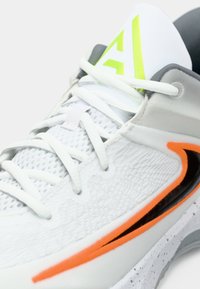 Λευκό αθλητικό παπούτσι με υφασμάτινη επάνω επιφάνεια, πορτοκαλί και μαύρες λεπτομέρειες, καθώς και μαξιλαρωμένο κολάρο. Οι κορδόνες είναι επίπεδες και ανοιχτό γκρι, με νεον λεπτομέρειες.