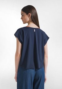 Tmavě modrý top s krátkými rukávy a pohodlným střihem, zaobleným lemem a malou štítkovou značkou na zadním výstřihu. Ležérní textura bavlněné látky.