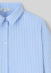 Chemise ample bleu clair à boutons avec des rayures verticales blanches, dotée d'un col classique et d'une texture de tissu lisse.