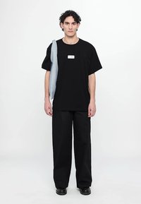 T-shirt noir oversize avec un petit logo blanc, associé à un pantalon large noir. Un sweat-shirt bleu clair est drapé sur une épaule.
