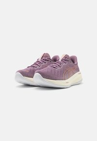 Zapatillas deportivas moradas con parte superior texturizada, acentos claros y suela blanca. Presentan una punta redondeada y elementos de diseño en contraste.