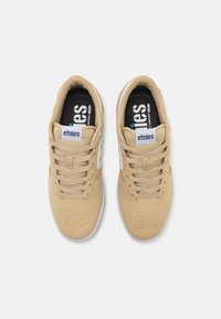 Beige sneakers with textured suede upper, white accents, and black insoles. Features round toe and perforated details for breathability.