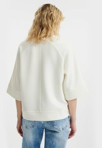 Felpa color crema con vestibilità rilassata, maniche ampie e orlo arrotondato, realizzata in tessuto morbido e caratterizzata da dettagli di cucitura minimi.