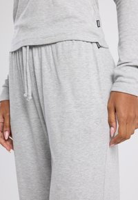 Lichtgrijze, geribbelde loungewear set bestaande uit een langemouwen top en broek met elastische tailleband. Opvallende details zijn de logo-accenten op beide stukken.