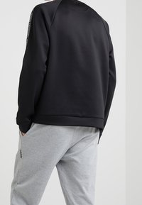 Felpa nera con una texture liscia, collo rotondo e maniche raglan. Abbinata a pantaloni della tuta grigi con un logo sul davanti.