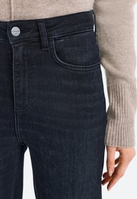 Vysoké tmavomodré džínsy vyrobené z denimu, s prednou vreckom, kovovým gombíkom na zapínanie a miernym elastanom pre lepšie padnutie.