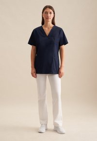 Divise da medico navy con scollo a V, maniche corte, dotate di tasca sul petto. Abbinato a pantaloni bianchi a gamba dritta e scarpe bianche.