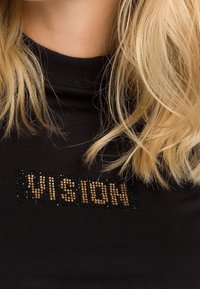 Czarny sweter z golfem z nadrukiem tekstowym "VISION" ozdobionym złotymi i czarnymi kamieniami. Miękka tkanina, dopasowany krój, minimalna tekstura.
