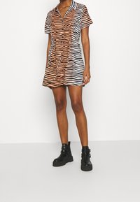 Šaty s krátkým rukávem s oranžovými a černými pruhy zebry, zapínání na knoflíky s límečkem, zúžený pas a uvolněný střih nad kolena.