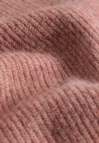 Kudotut kankaat, pehmeässä ruusuvärissä, joissa on uritettu rakenne ja pörröinen pinta. Lähikuvassa näkyvät hienot langan yksityiskohdat ja kerrokset.