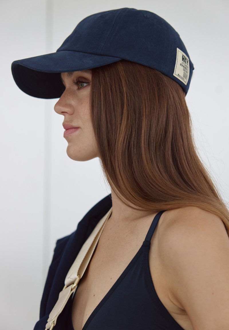 Casquette bleu marine avec une visière incurvée, en coton. Dotée d'une étiquette de patch avec du texte à l'arrière. Texture lisse et design simple.