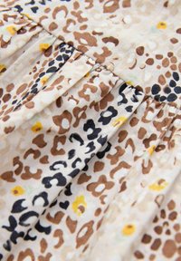 Tessuto leggero con uno sfondo beige e un mix di macchie leopardate marroni, nere e gialle. La texture plissettata aggiunge dimensione.