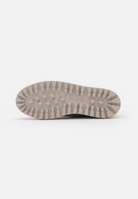 Semelle de chaussure en matériau caoutchouteux beige, affichant un motif texturé avec des crampons et des rainures prononcés pour une meilleure adhérence.