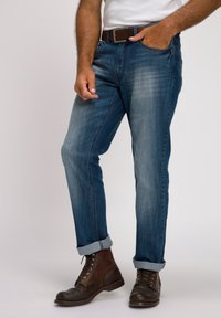 Pantalones vaqueros de denim azul con corte recto, ligero desgaste, puños doblados y bolsillos delanteros, combinados con botas de cuero marrón con cordones.