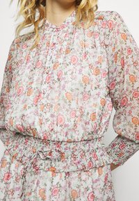 Kwiecista sukienka z lekkiego, przejrzystego materiału w pastelowych kolorach. Posiada marszczony pas, długie rękawy oraz zapinany z przodu na guziki wzór z różnymi kwiatami.