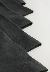Mörkgrått tyg med veckade ärmar, med en slät textur och ren sömnad. Materialet verkar mjukt och lätt.
