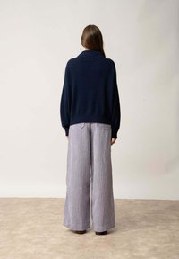 Granatowy sweter dzianinowy z wysokim kołnierzem i luźnym krojem, w połączeniu z szerokimi spodniami w paski w jasnym fiolecie i bieli.