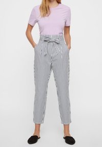 T-shirt à manches courtes violet clair associé à un pantalon taille haute rayé noir et blanc avec une ceinture nouée et des poches latérales.