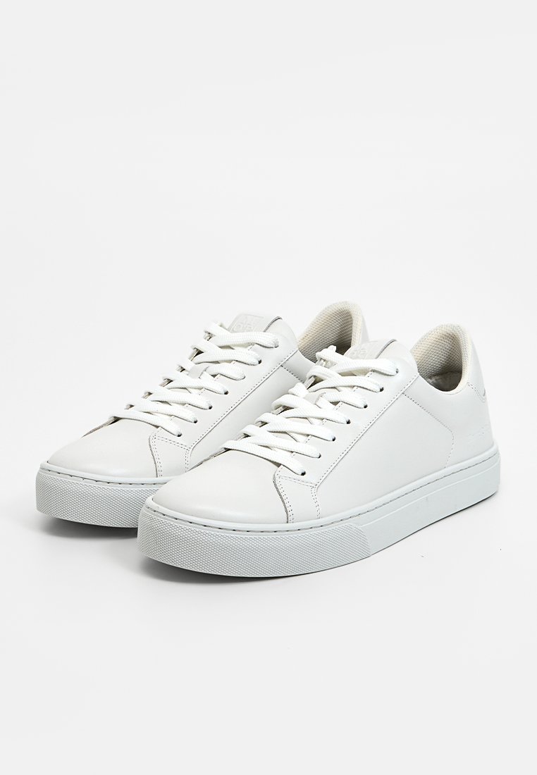 Weiße Ledersneaker mit glatter Oberfläche, runder Spitze, flachen Schnürsenkeln und strukturierten Gummisohlen. Minimalistisches Design ohne sichtbare Markenkennzeichnung.