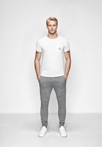 Hvid T-shirt med gul kant og en brystlomme, parret med grå træningsbukser. Hvide sneakers fuldender outfittet. Minimalistisk design.