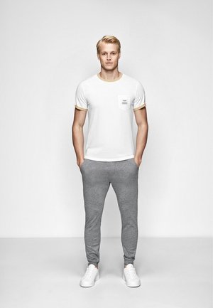 Hvid T-shirt med gul kant og en brystlomme, parret med grå træningsbukser. Hvide sneakers fuldender outfittet. Minimalistisk design.