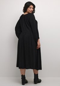 Black dress featuring a textured fabric, long sleeves, and a keyhole back detail, with a flowy skirt and paired with black ankle boots.