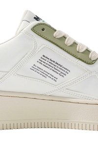 Białe syntetyczne sneakersy z teksturowaną kremową podeszwą, zielonymi akcentami oraz etykietą opisującą materiały przyjazne dla środowiska i filozofię marki.