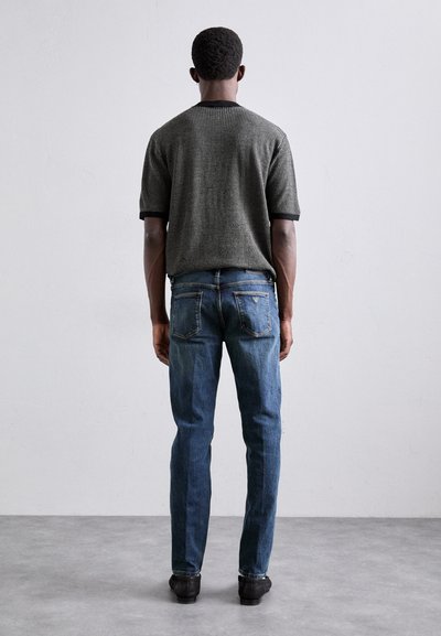 Camicetta a maniche corte in bianco e nero con trama, colletto a coste, abbinata a jeans in denim blu e mocassini neri intrecciati.