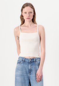 Ribovaná, krémově bílá crop top s tenkými ramínky. Má čtvercový výstřih a přiléhavý střih. Vytvořeno s světle modrými džíny s vysokým pasem.