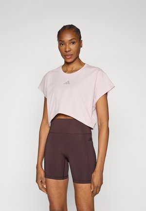 Lyserød cropped t-shirt med korte ærmer og et lille logo foran, kombineret med brune cykelshorts med høj talje.