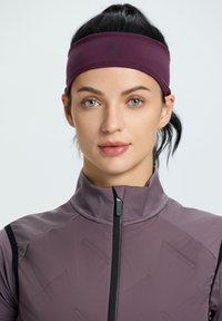 Violetti panta, joka on valmistettu venyvästä materiaalista ja jossa on huomaamaton logo. Mallilla on päällään vetoketjullinen takki, joka on vaaleammassa violettisävyssä.