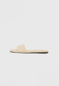 Beige flache Rutsch-Sandale mit einem breiten Einzelriemen, glattem Leder-Obermaterial, gepolstertem Fußbett und einem minimalistischen Design mit dünner Sohle.
