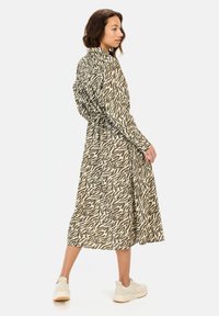 Groene en beige gestreepte midi-jurk met lange mouwen, een taille met trekkoord en een relaxte pasvorm. Draag met witte sneakers.