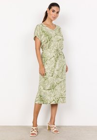 Grünes und weißes Kleid mit Blättermuster, kurze Ärmel, lockere Passform, tailliert, knielang, getragen mit hellen Blockabsätzen.