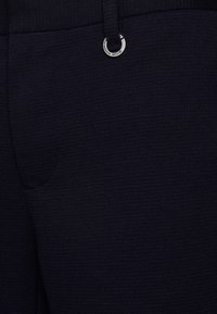 Navy blue pants with a textured fabric, featuring a front pocket and a metal ring accent on the waistband.