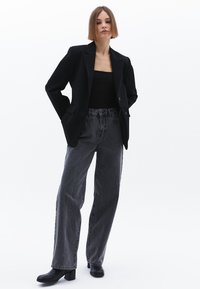 Blazer noir avec revers et poches, porté sur un haut noir. Jean gris taille haute à coupe ample. Bottines noires à talons.