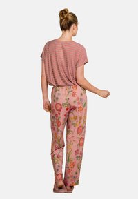 Gestreiftes rot-weißes Kurzarmoberteil, kombiniert mit rosa, floral bestickten Hosen, die grüne Blätter aufweisen und einen lockeren Schnitt haben.