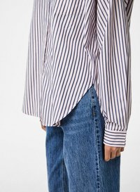 Camicia a righe button-up nei toni rosa e blu navy, con maniche lunghe e orlo arrotondato, dotata di una tasca sul petto, abbinata a jeans in denim blu.