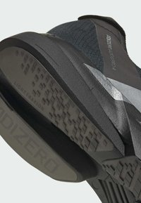 Black and gray athletic shoe with a textured upper, distinctive serrated design on a cushioned sole, featuring "LIGHTTRAXION" branding.