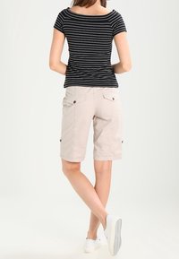 Haut à manches courtes rayé noir et blanc assorti à un short beige clair arrivant au genou. Le short comporte deux poches arrière et des boutons décoratifs.