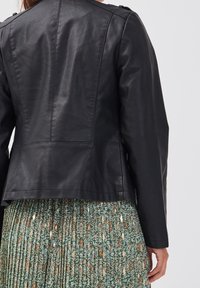 Veste en cuir noir avec une texture lisse, épaules structurées et coutures subtiles, associée à une jupe plissée à motifs floraux verts.