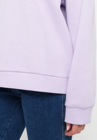 Λαχανί φούτερ με ριμπ μανσέτες και στρίφωμα, κατασκευασμένο από μαλακό βαμβακερό ύφασμα, σε συνδυασμό με σκούρα μπλε τζιν παντελόνι.