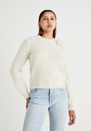 Cream-colored knitted sweater with a round neckline, ribbed cuffs, and hem, featuring a floral accent on the left shoulder.